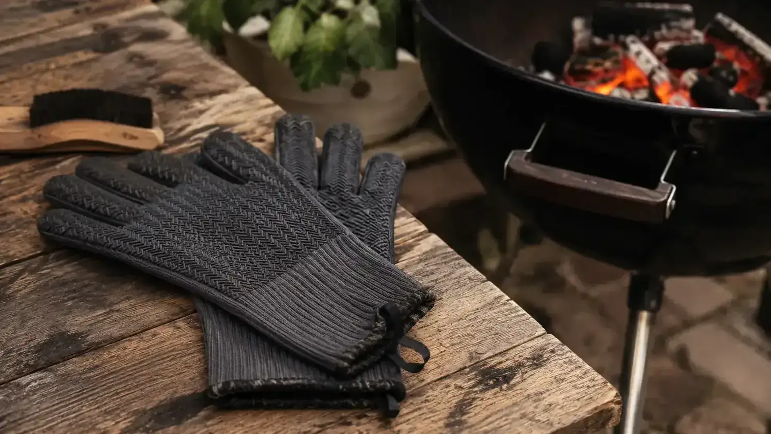 Pair of red and black RAPICCA BBQ gloves resting on a cast iron grate with glowing charcoal below